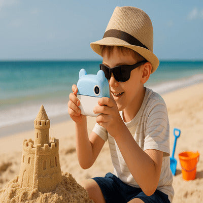 Garçon utilisant un appareil photo enfant pour photographier son chùteau de sable sur la plage pendant les vacances